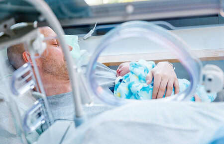 Vater mit Neugeborenem im Arm beim Kangarooing auf der Neonatoalogie